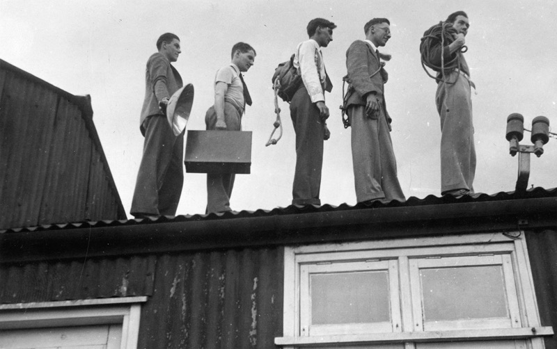 Five climbers walking a rooftop ridge with ropes and flash equipment